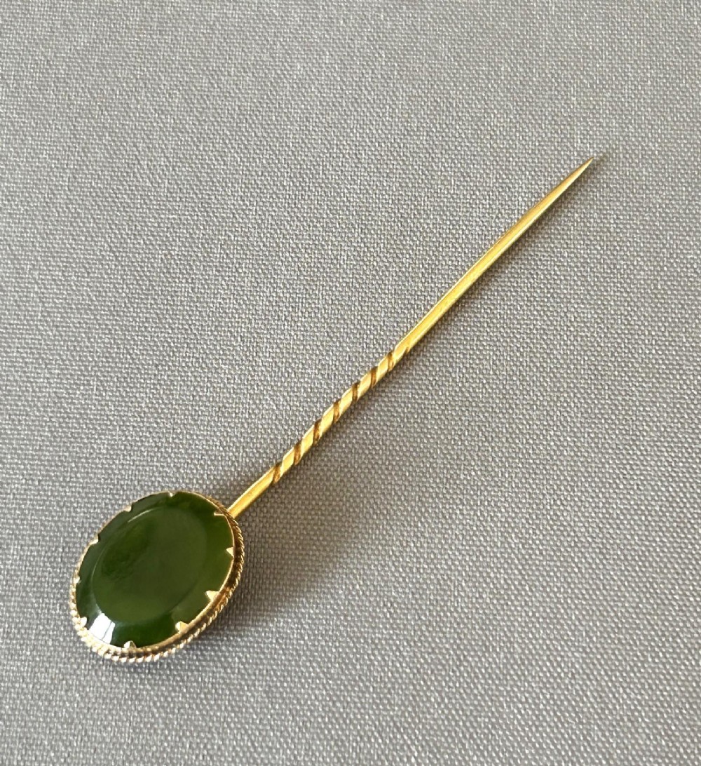 An Edwardian 9ct gold stick pin featuring an oval green jade cabochon set above a twisted gold stem. View VI