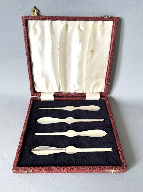 A set of four silver crab picks arranged inside a navy velvet and white silk lined burgundy presentation box.