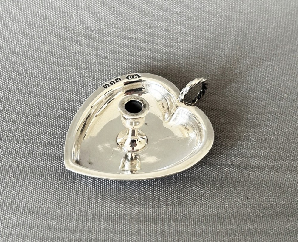A heart-shaped Victorian sterling silver miniature chamberstick go-to-bed featuring a central socket, a twisted wire loop handle, and visible hallmarks.