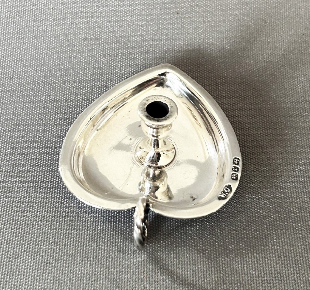 A heart-shaped Victorian sterling silver miniature chamberstick go-to-bed featuring a central socket, a twisted wire loop handle, and visible hallmarks. View V