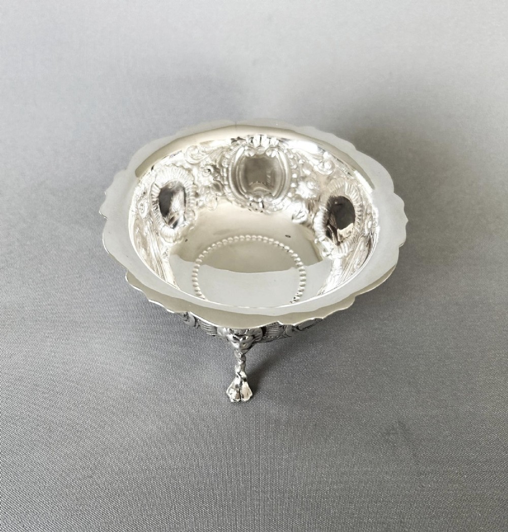 A circular silver bowl featuring embossed goat motifs, floral repousse decoration, a scalloped rim, and three sculptural mask feet. View II