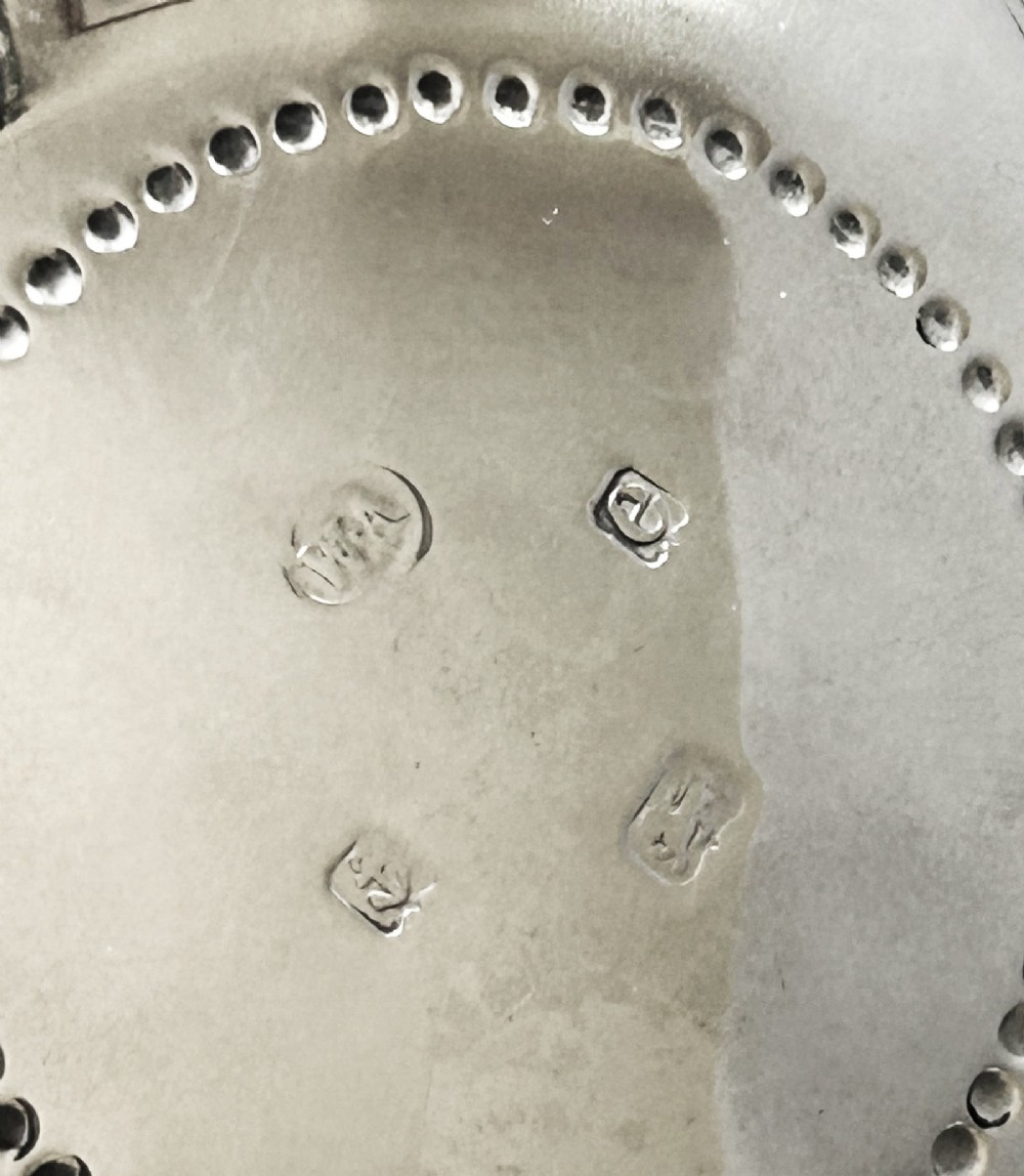 A circular silver bowl featuring embossed goat motifs, floral repousse decoration, a scalloped rim, and three sculptural mask feet. View VII