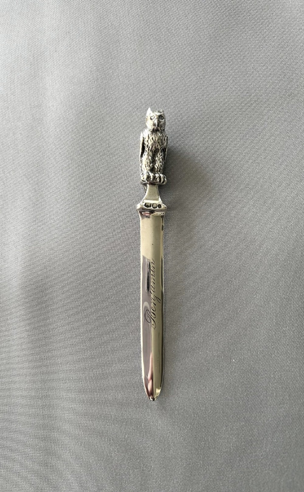 A silver letter opener featuring a finely cast owl handle above a polished blade engraved with script text.