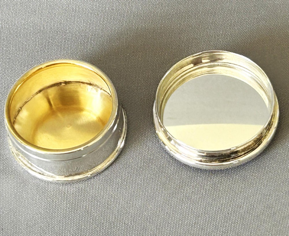 A circular sterling silver pillbox featuring engraved scrollwork on the lid surrounding four inlaid dark green agate stones. View IV