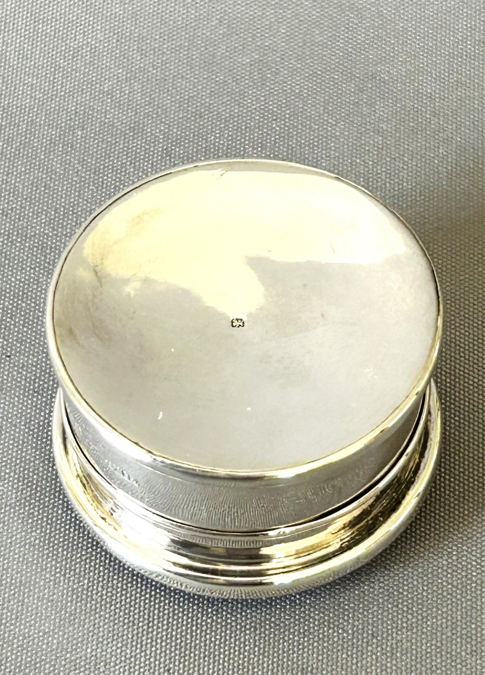 A circular sterling silver pillbox featuring engraved scrollwork on the lid surrounding four inlaid dark green agate stones. View V