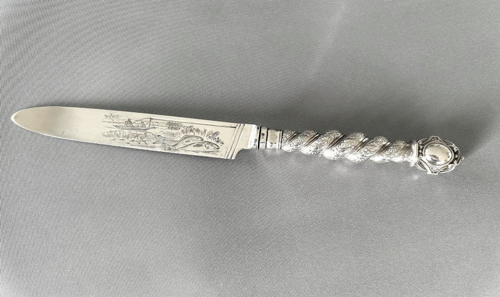 A Victorian silver fish serving knife featuring an engraved river landscape scene on the blade and a chased spiral twist handle.