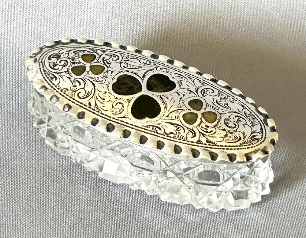 An oval Edwardian cut glass trinket box featuring an engraved sterling silver lid inset with green Connemara marble shamrock shapes.