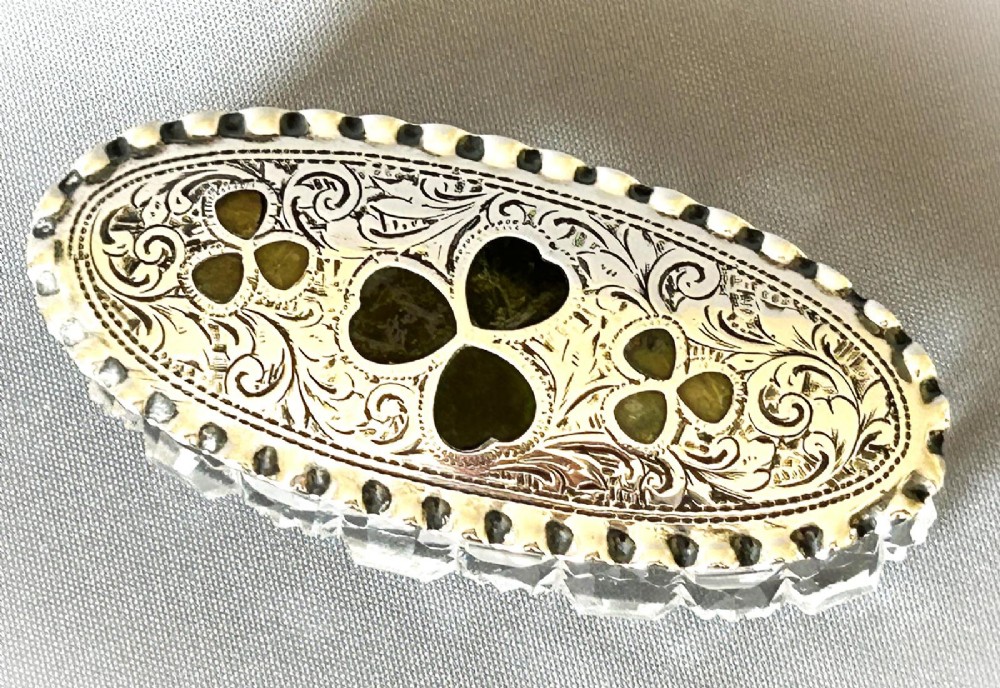 An oval Edwardian cut glass trinket box featuring an engraved sterling silver lid inset with green Connemara marble shamrock shapes. View VI
