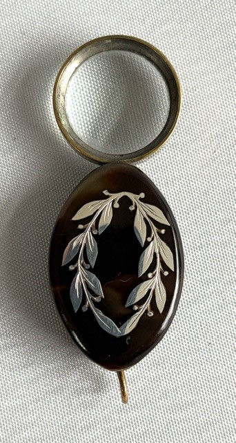 A Victorian oval dark brown tortoiseshell folding loupe decorated with silver pique foliate inlay and featuring a swivelling circular magnifying glass lens.