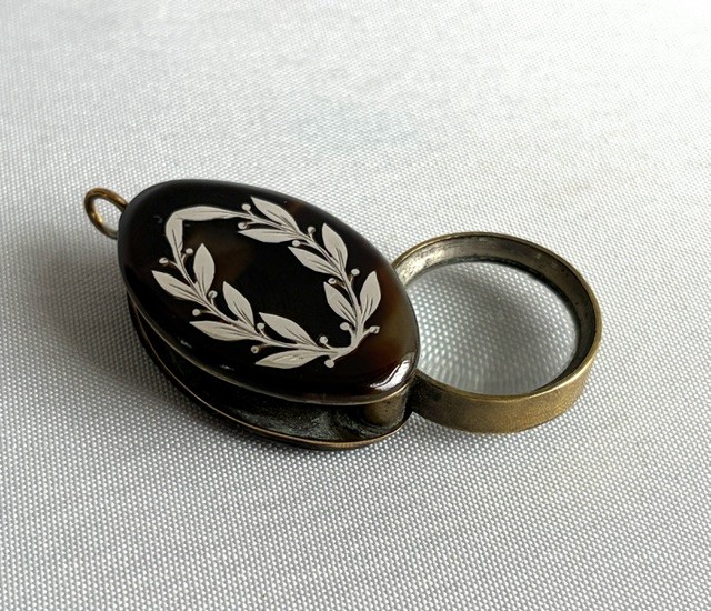 A Victorian oval dark brown tortoiseshell folding loupe decorated with silver pique foliate inlay and featuring a swivelling circular magnifying glass lens. View IV