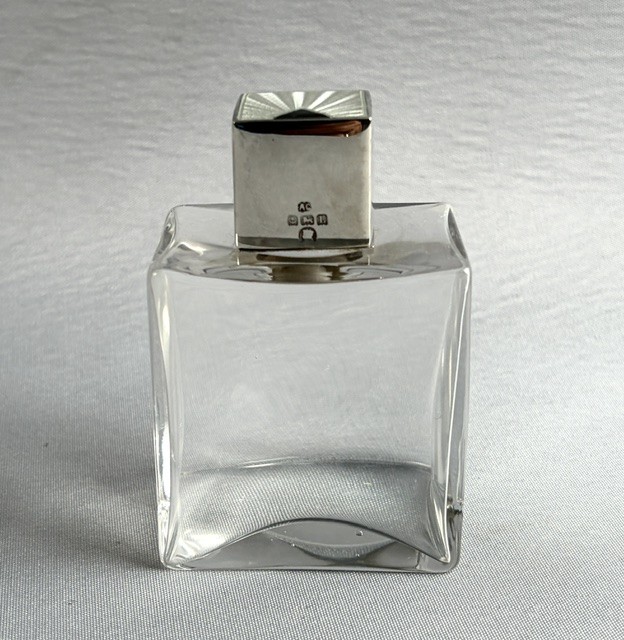 An Art Deco clear glass cologne bottle featuring a cubic silver cap with engine-turned sunburst detailing. View II