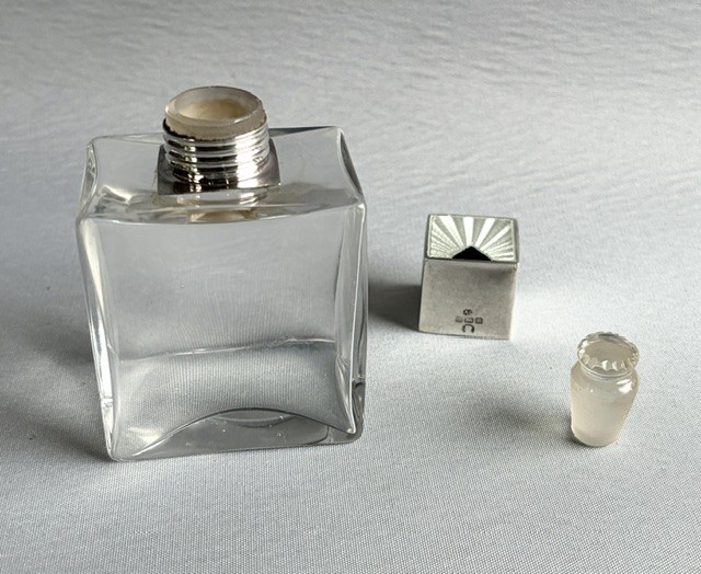 An Art Deco clear glass cologne bottle featuring a cubic silver cap with engine-turned sunburst detailing. View VI