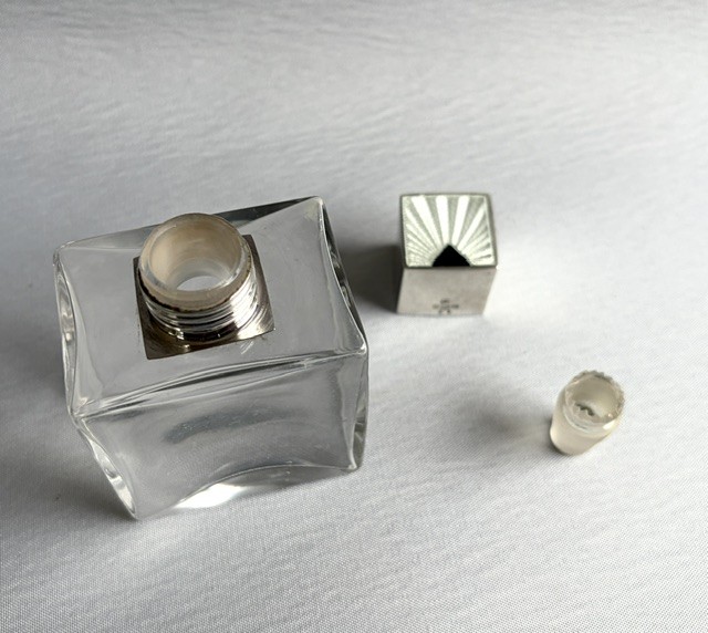 An Art Deco clear glass cologne bottle featuring a cubic silver cap with engine-turned sunburst detailing. View VII