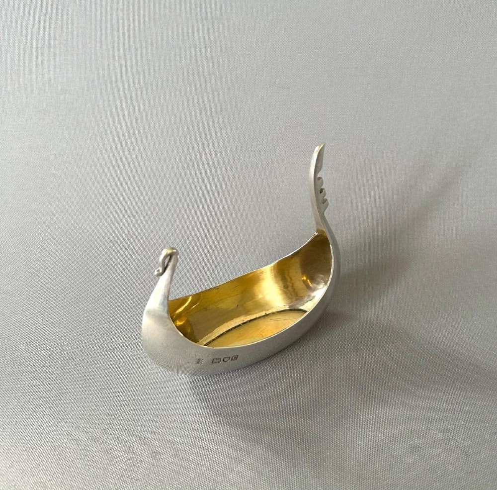 A Victorian sterling silver salt tub fashioned in the shape of a boat with a gilded interior and visible hallmarks on the exterior side. View VI