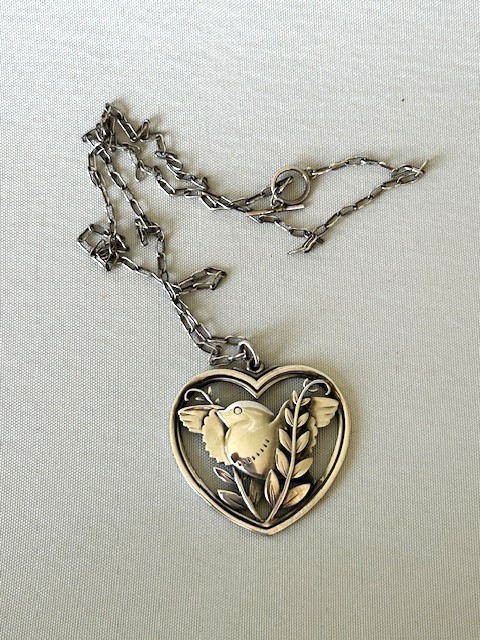 A sterling silver heart-shaped pendant featuring a pierced bird and foliage motif suspended from a link chain.