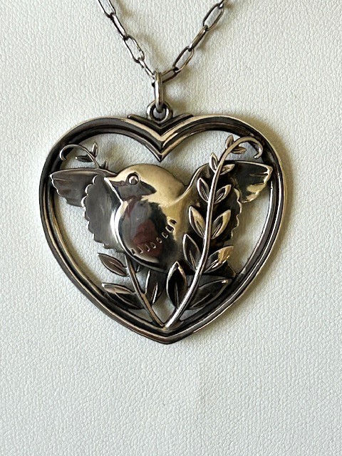 A sterling silver heart-shaped pendant featuring a pierced bird and foliage motif suspended from a link chain. View V