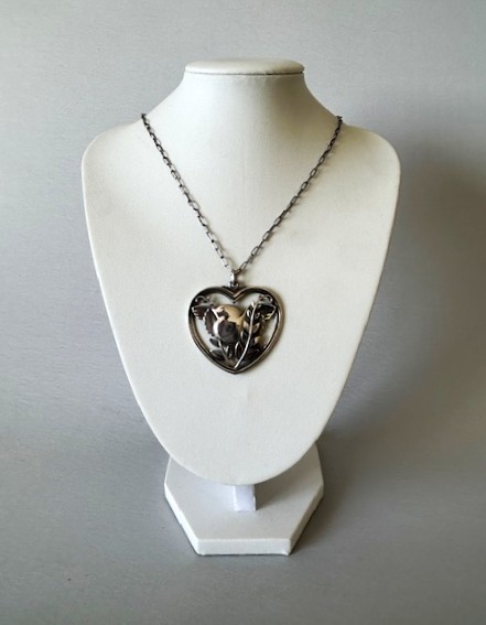 A sterling silver heart-shaped pendant featuring a pierced bird and foliage motif suspended from a link chain. View VI