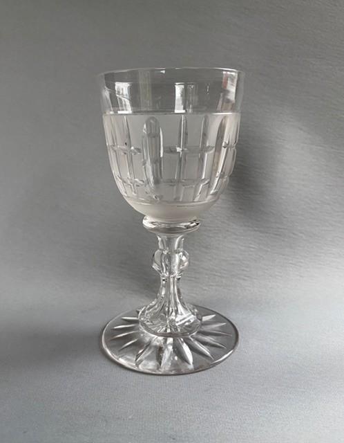 A clear Victorian cut crystal wine goblet featuring a frosted geometric pattern, faceted stem, and star-cut base.