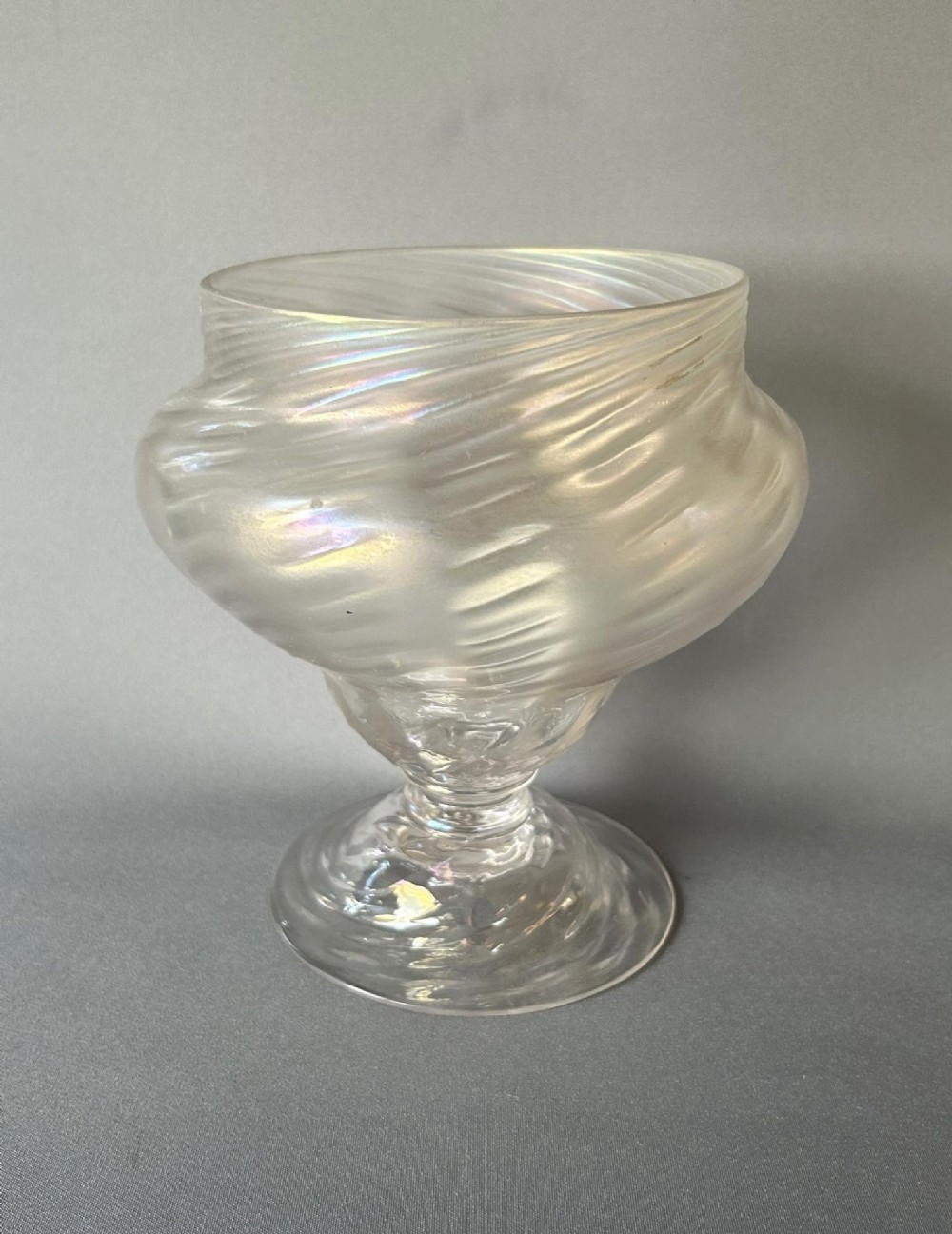 An Art Nouveau clear glass pedestal vase featuring a spiralled rib design and an iridescent lustre finish.