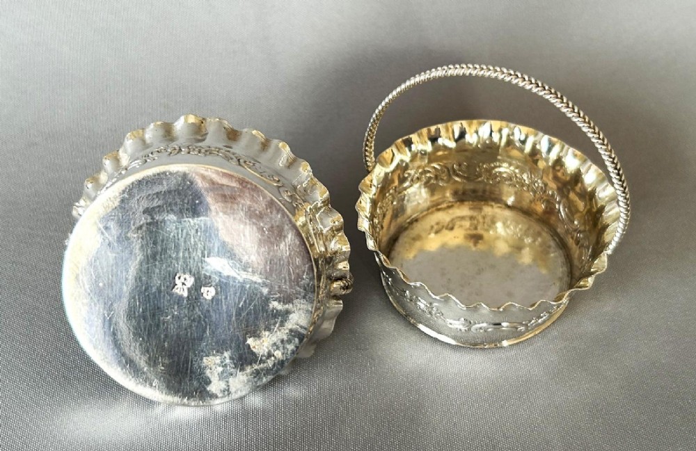 A pair of small silver bonbon baskets featuring crimped rims, embossed scrollwork motifs, and twisted overhead rope handles. View II
