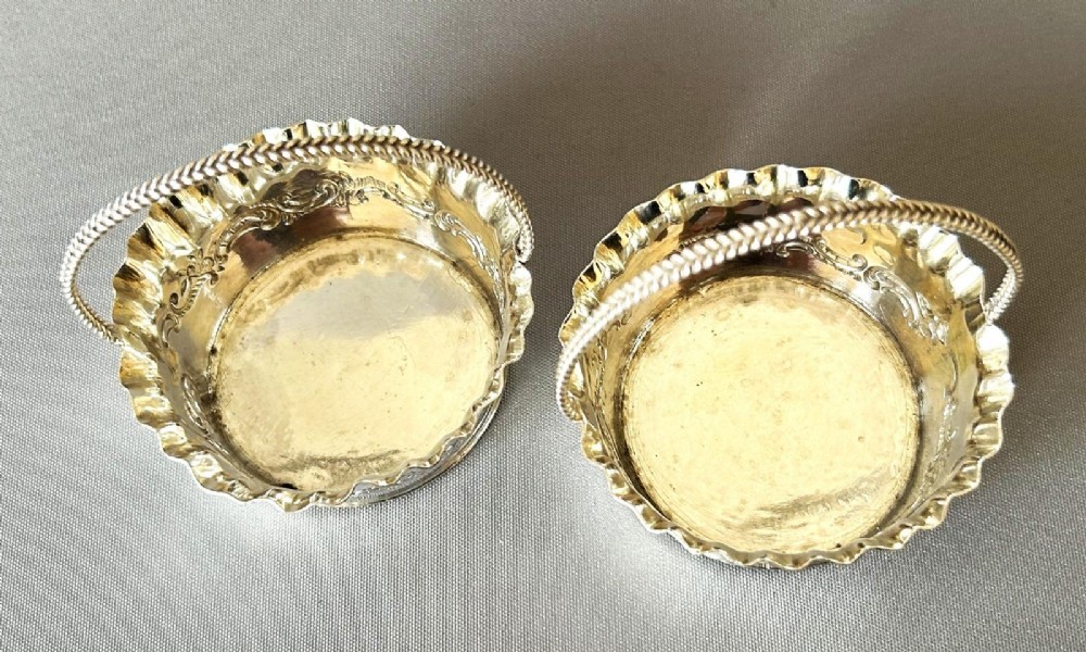 A pair of small silver bonbon baskets featuring crimped rims, embossed scrollwork motifs, and twisted overhead rope handles. View VII