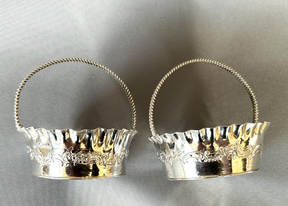 A pair of small silver bonbon baskets featuring crimped rims, embossed scrollwork motifs, and twisted overhead rope handles. View VIII