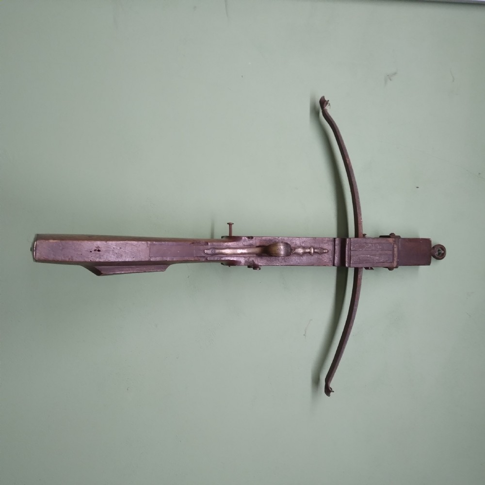 An antique wooden crossbow featuring a carved dark timber stock, a curved iron bow prod, and brass trigger embellishments.