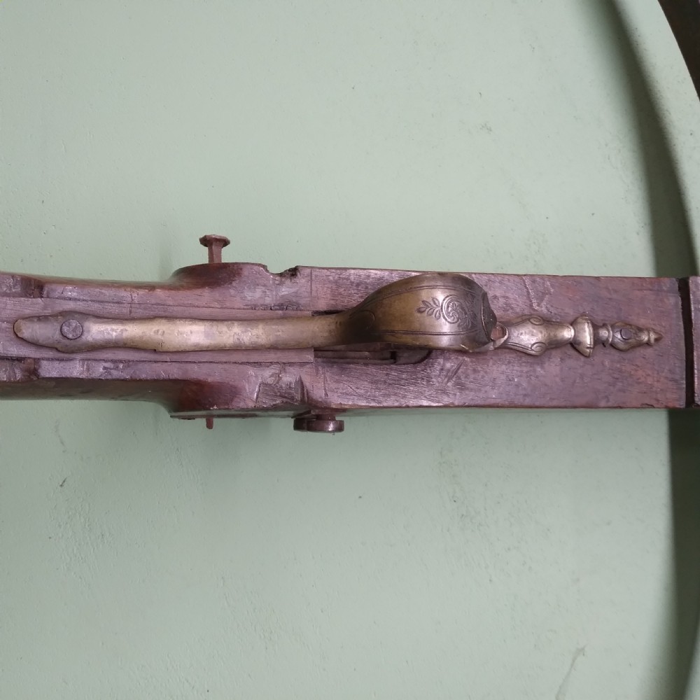 An antique wooden crossbow featuring a carved dark timber stock, a curved iron bow prod, and brass trigger embellishments. View II