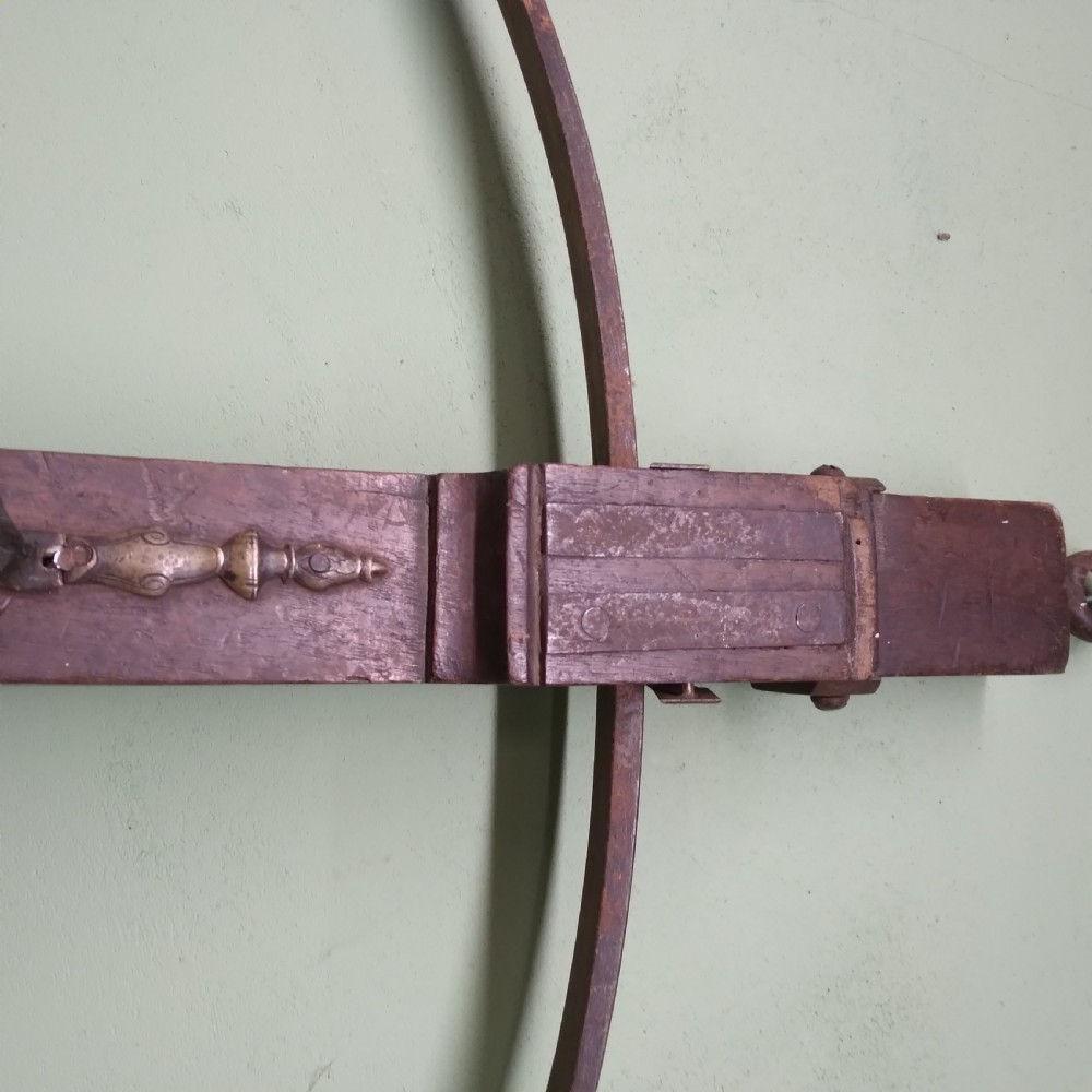 An antique wooden crossbow featuring a carved dark timber stock, a curved iron bow prod, and brass trigger embellishments. View III