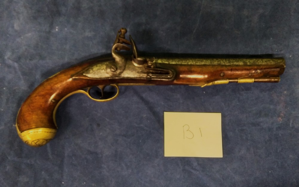 An 18th-century flintlock pistol featuring a carved walnut stock, a dark steel lock mechanism, and a rounded brass butt cap.