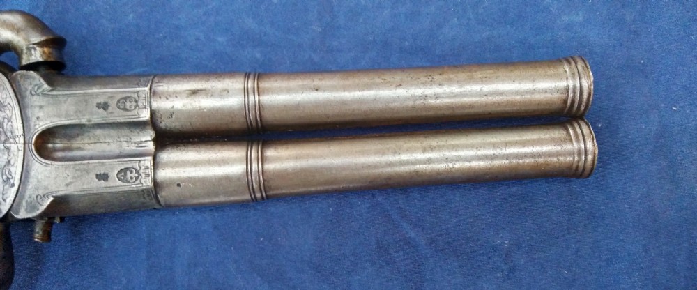 An early 19th-century revolving barrel pistol featuring twin steel barrels, an engraved lockplate, and a curved wooden grip. View VI