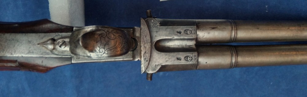 An early 19th-century revolving barrel pistol featuring twin steel barrels, an engraved lockplate, and a curved wooden grip. View X