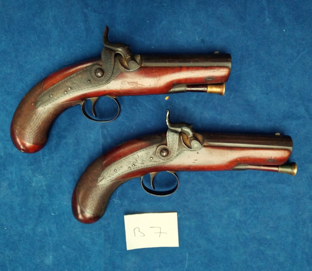 A matched pair of 19th-century percussion cap pistols featuring chequered walnut stocks, engraved steel lockplates, and brass-tipped ramrods.