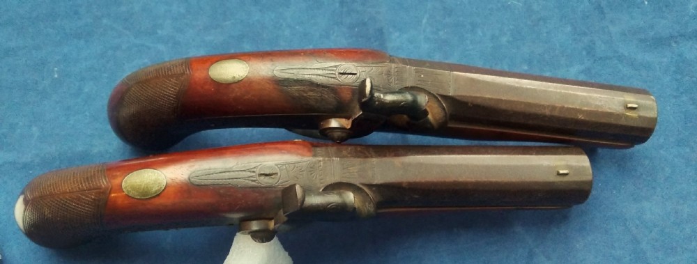 A matched pair of 19th-century percussion cap pistols featuring chequered walnut stocks, engraved steel lockplates, and brass-tipped ramrods. View V