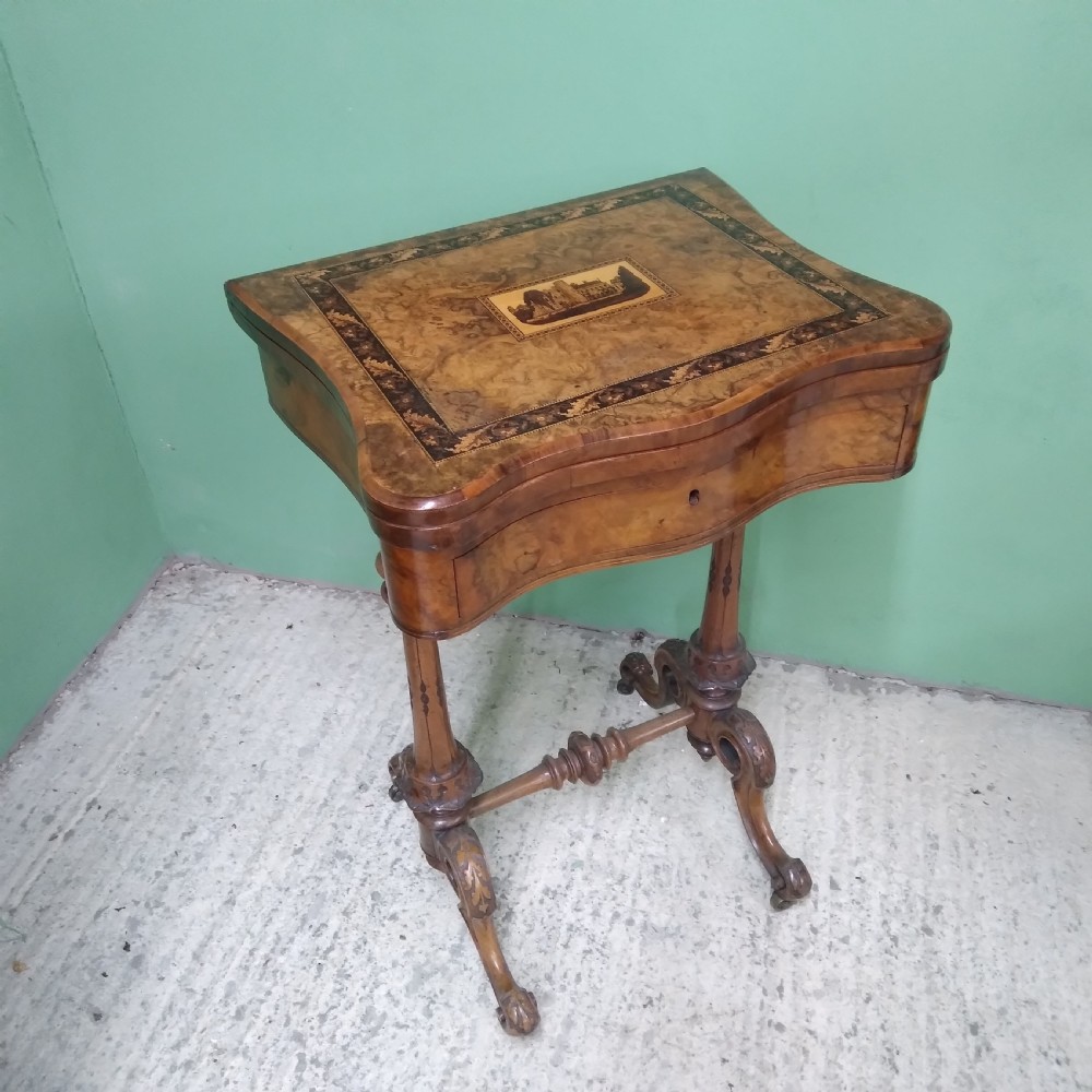 A Victorian burr walnut work table featuring a central Tunbridge ware marquetry landscape scene, serpentine edges, and turned legs with scroll feet.