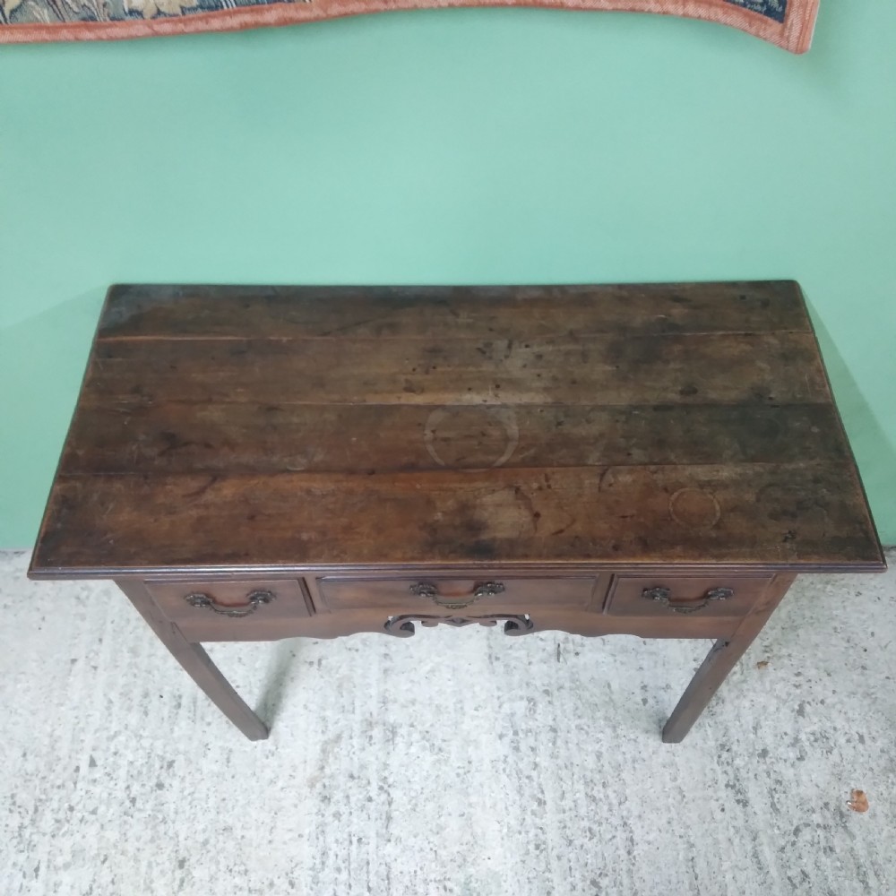 An antique fruitwood lowboy table featuring three drawers with brass drop handles, a shaped lower apron, and four square legs. View IV