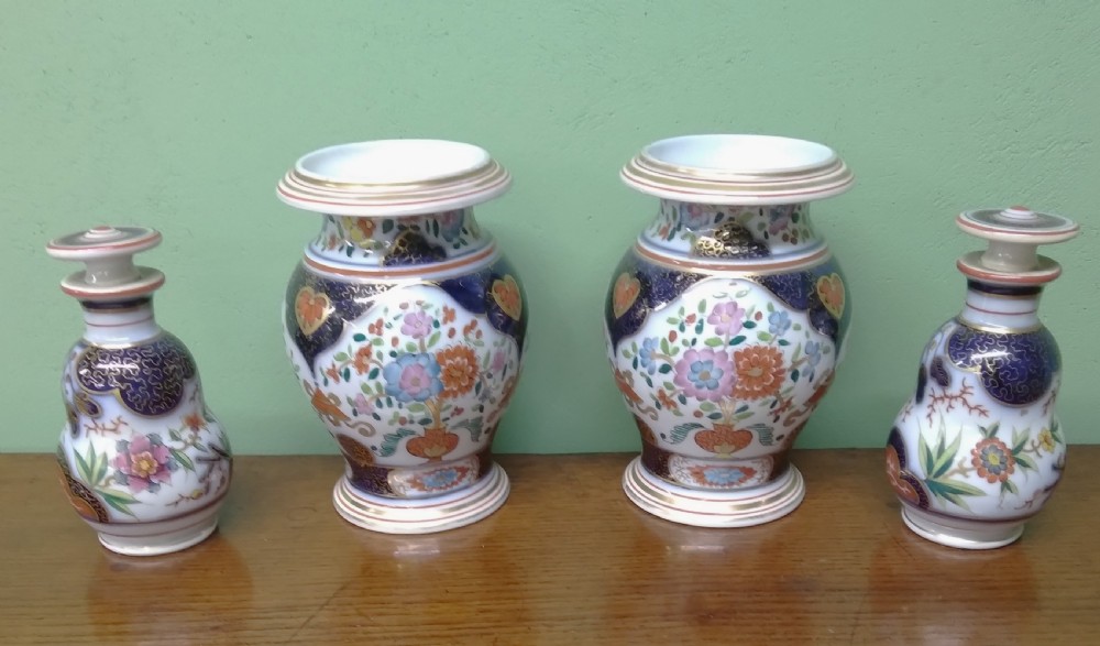 A four-piece antique Continental porcelain garniture set featuring two central urn-shaped vases and two outer stoppered bottles with cobalt blue panels and polychrome floral decoration.