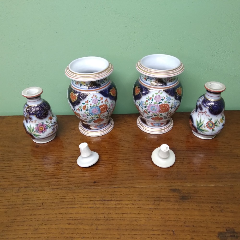 A four-piece antique Continental porcelain garniture set featuring two central urn-shaped vases and two outer stoppered bottles with cobalt blue panels and polychrome floral decoration. View IV