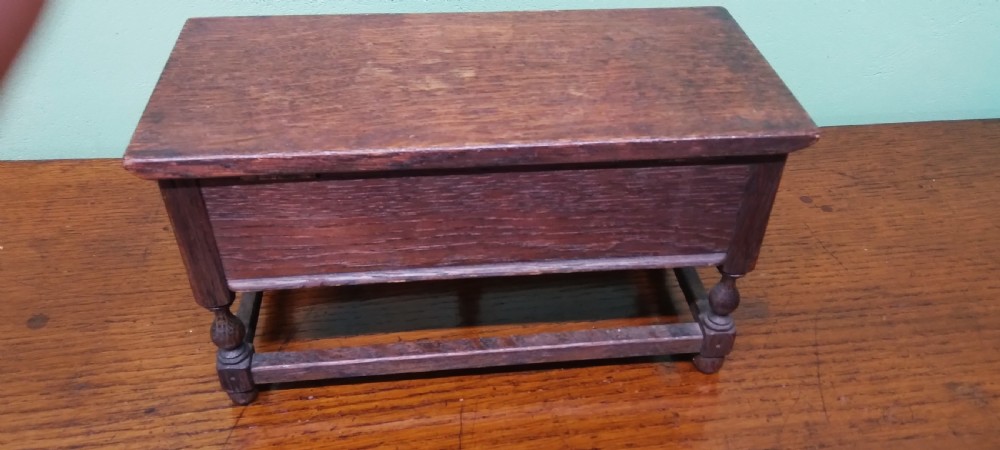 A small dark oak miniature dresser featuring four carved geometric panel fronts, small wooden knob handles, turned legs, and a bottom stretcher rail. View III