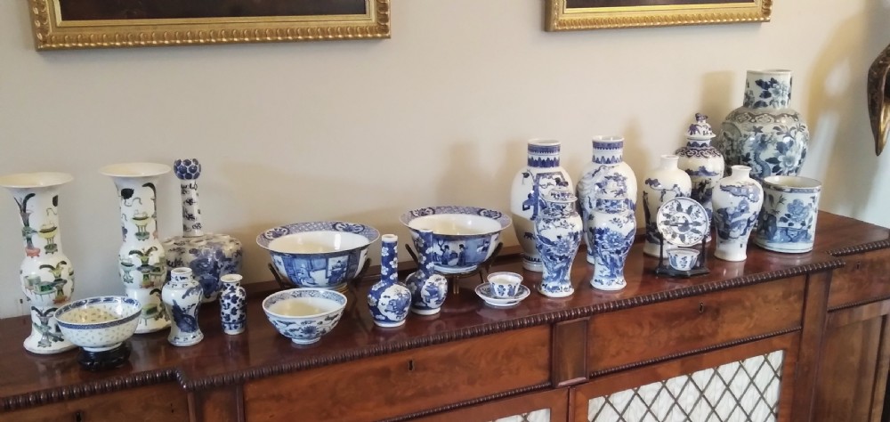 A collection of varied Chinese blue and white and polychrome porcelain vases, bowls, and jars displayed along a dark wood sideboard.
