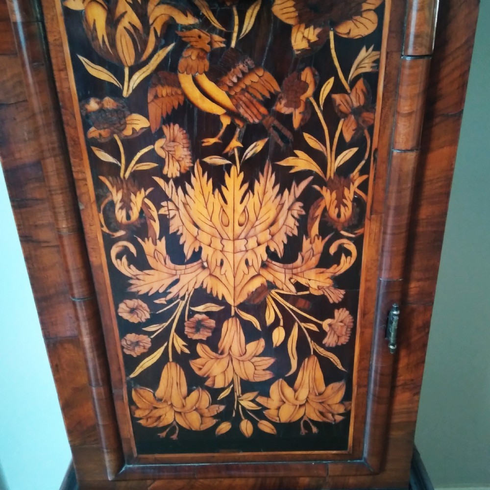 A 17th-century walnut longcase clock featuring floral marquetry inlays, a square brass dial, and twisted hood columns. View VII