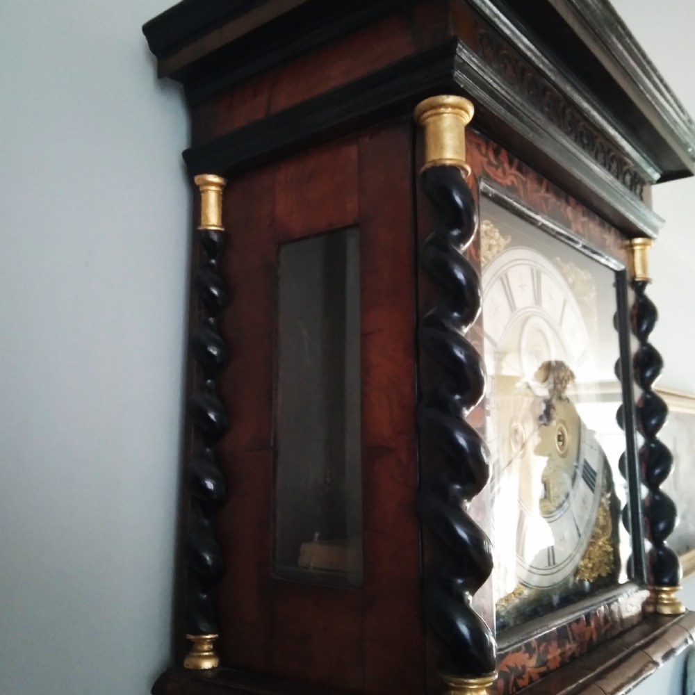 A 17th-century walnut longcase clock featuring floral marquetry inlays, a square brass dial, and twisted hood columns. View IX