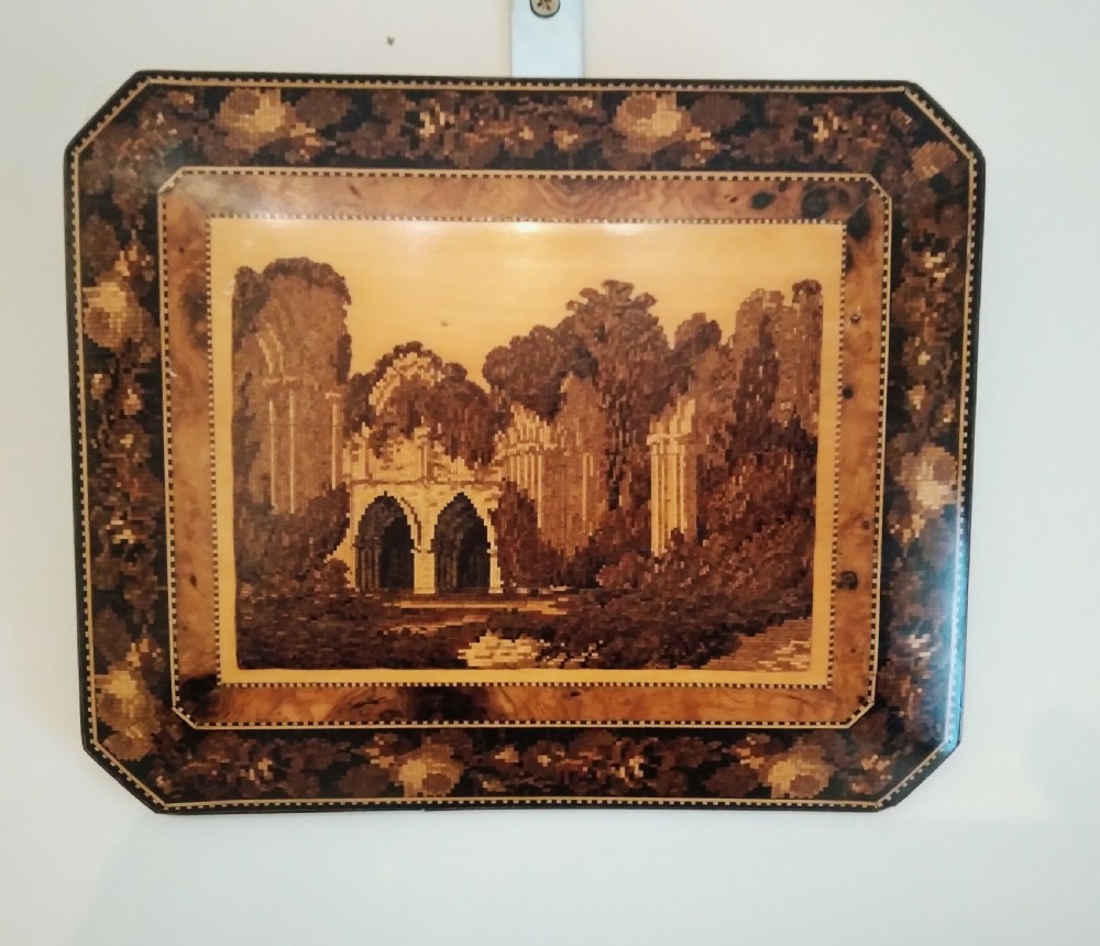 A rectangular Victorian Tunbridge ware wooden plaque featuring an inlaid mosaic picture of abbey ruins within floral and geometric borders.