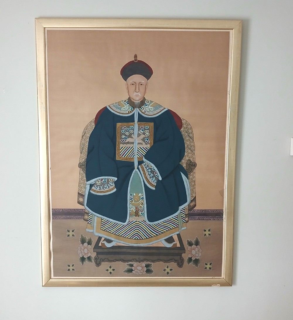A framed Chinese ancestor portrait depicting a seated figure in a dark blue official court robe with a rank badge and court hat.
