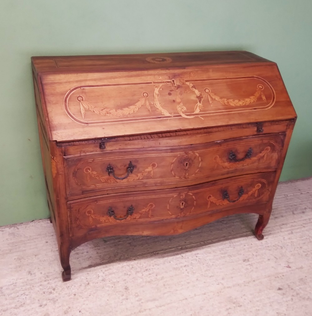 An 18th-century fruitwood writing bureau featuring a sloping fall-front lid with decorative marquetry garland inlays and two drawers below.