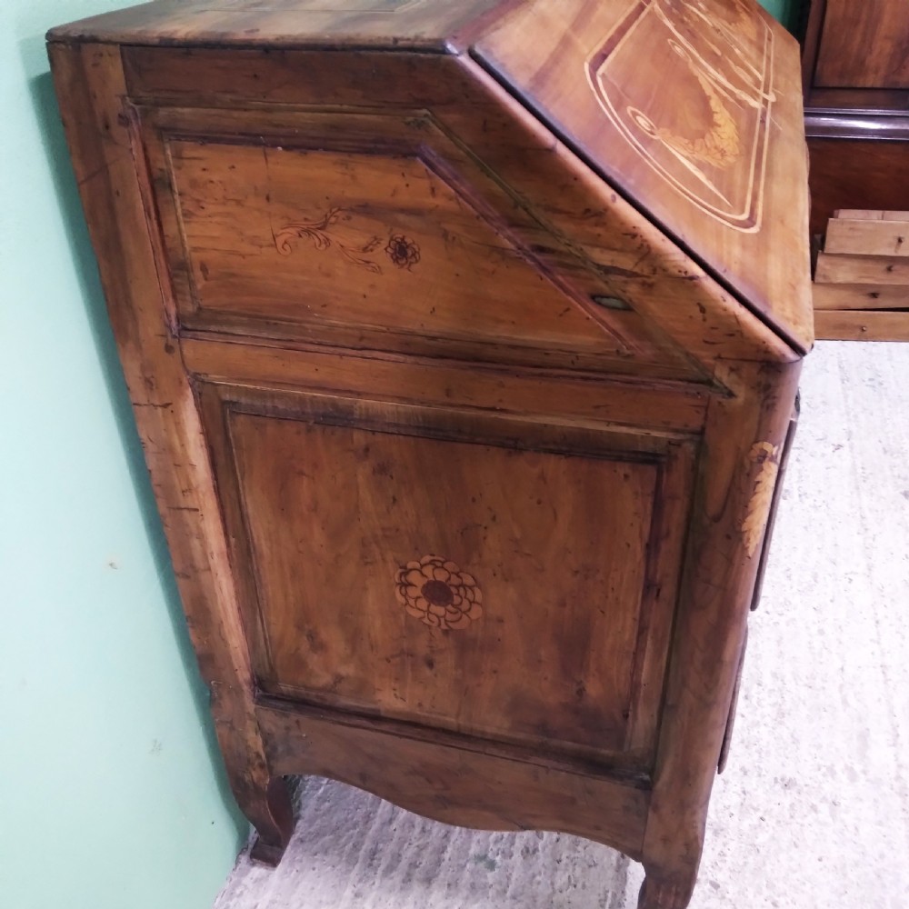 An 18th-century fruitwood writing bureau featuring a sloping fall-front lid with decorative marquetry garland inlays and two drawers below. View V