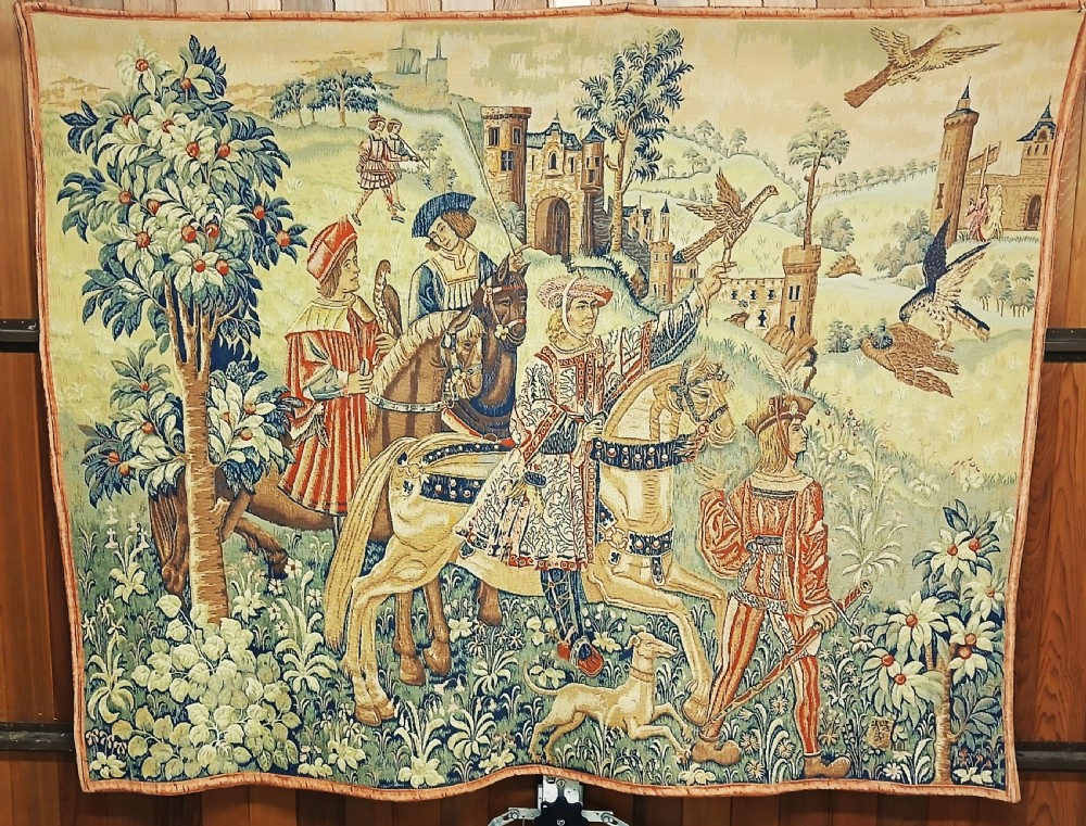 A late 19th-century woven wall tapestry depicting a medieval hawking scene with figures on horseback, falcons, hunting dogs, and a distant castle backdrop.