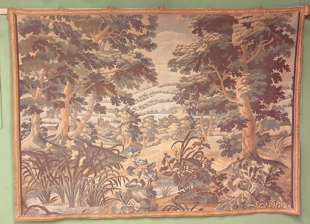 A late nineteenth-century French woven verdure tapestry depicting a dense forest landscape with trees, foreground foliage, and a distant castle under a cloudy sky.