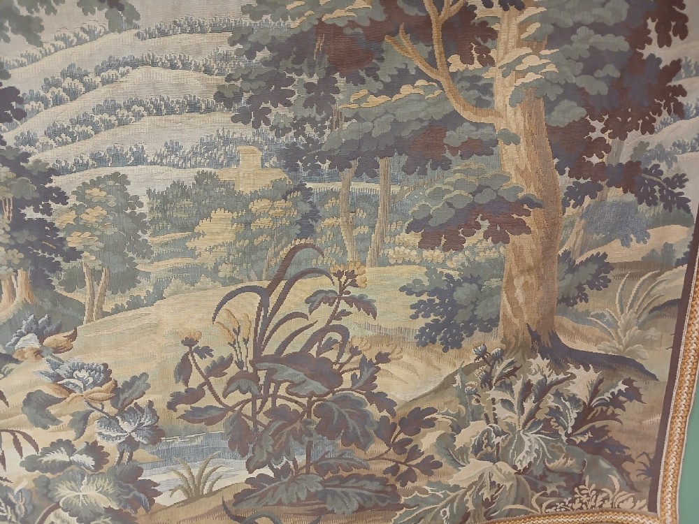 A late nineteenth-century French woven verdure tapestry depicting a dense forest landscape with trees, foreground foliage, and a distant castle under a cloudy sky. View III