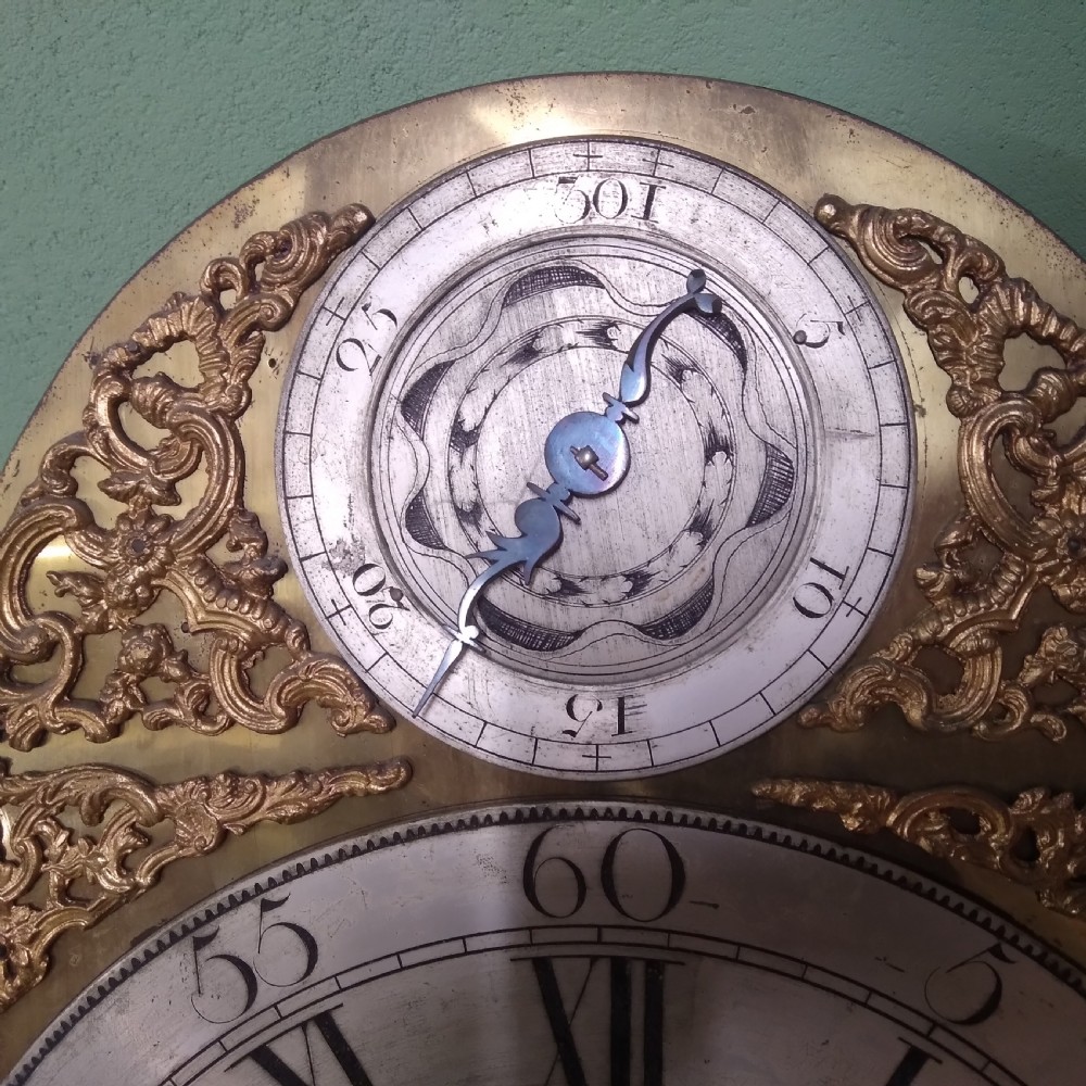 An 18th-century mahogany longcase clock featuring a swan-neck pediment, brass arch dial, and turned hood columns. View V